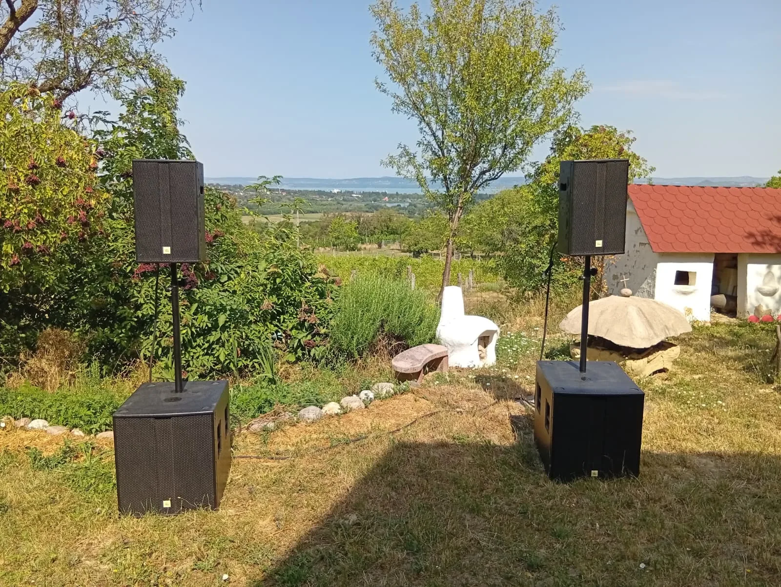 Komplettes Open-Air-Setup: zwei PA-Tops auf Stativen über Subwoofern in einem Garten