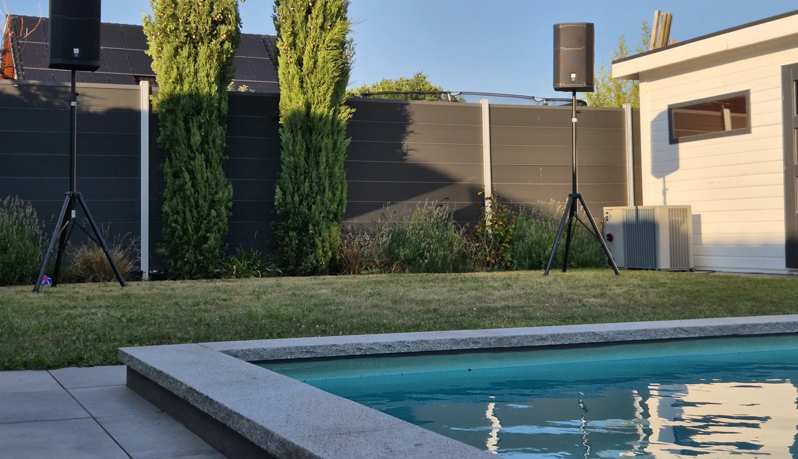 Zwei PA-Tops auf Stativen am Pool bei einer Gartenparty, aufgebaut auf dem Rasen neben dem Wasser