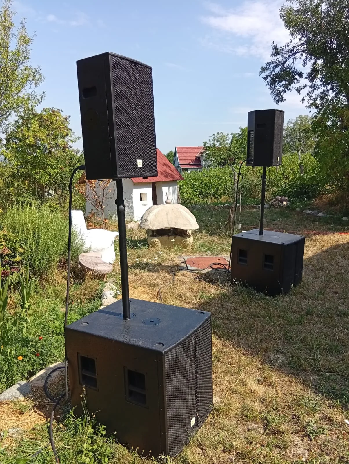 Zwei PA-Tops auf Stativen, jeweils über einem Subwoofer, aufgebaut für ein Open-Air-Event